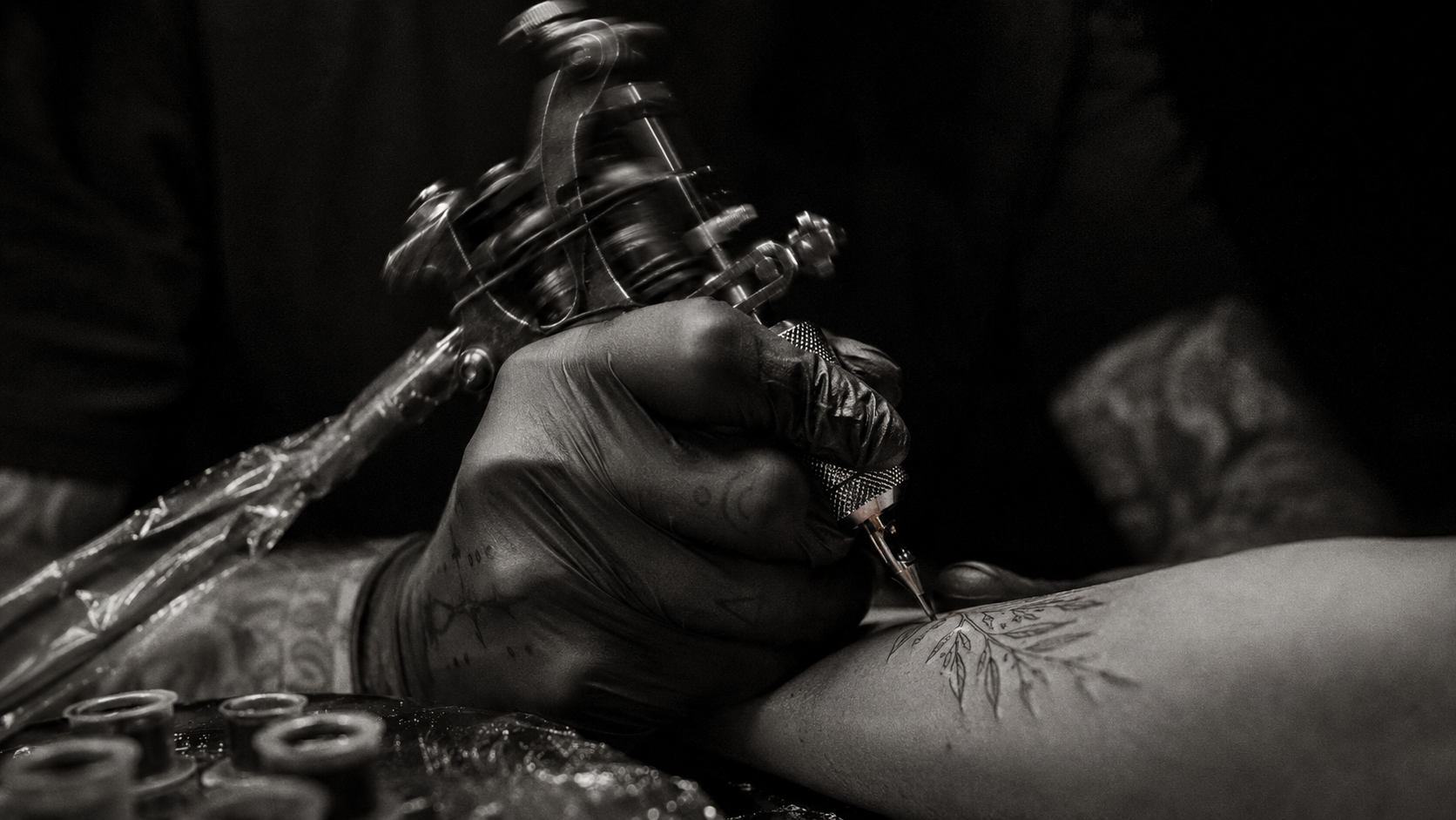 Black and white close-up of a hand holding a tattoo machine mid-work